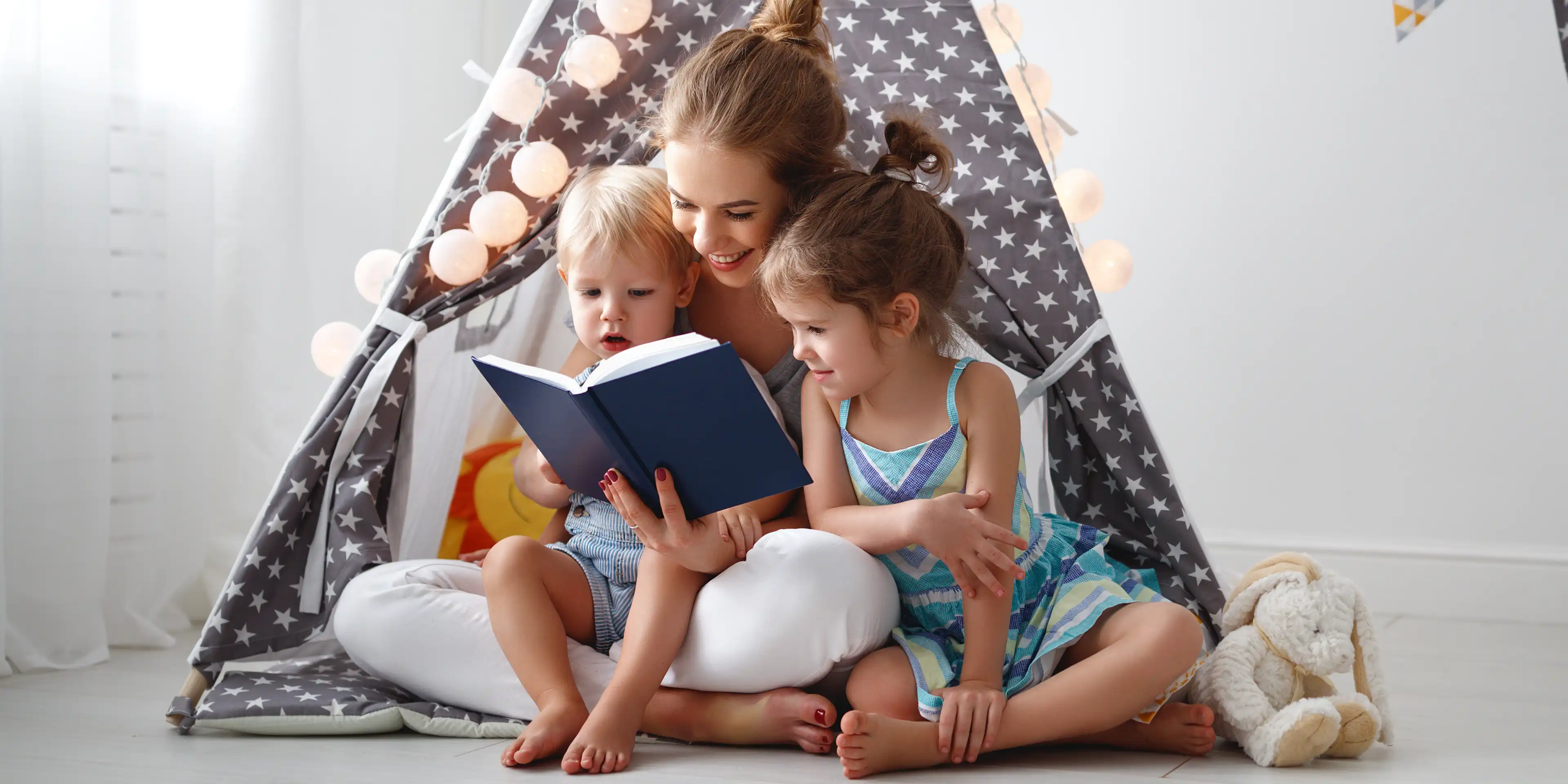 Caregiver reading to children in a cozy tent setting with soft lighting and toys